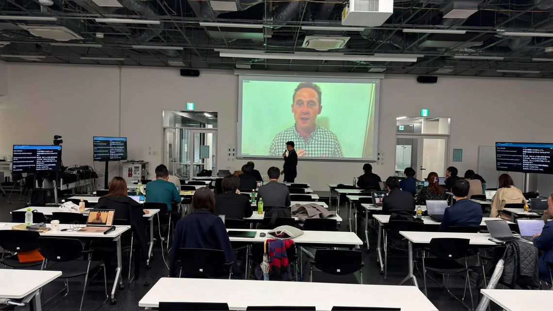 会場の左右に設置されたモニターに、日本語のリアルタイム通訳が表示されている様子